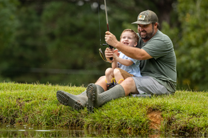 a man sitting by a river fishing with his son wearing Lite Boots